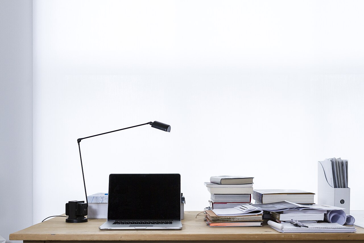 Laptop on desk book stacks (Unsplash)