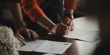 주황색 소매 셔츠를 입은 사람이 흰 문서에 필기하는 장면