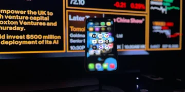 Smartphone displaying AI apps in front of a financial data screen in London.
