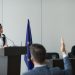 A woman speaking at a European Union conference while delegates listen attentively.