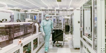 Scientist in protective gear walking in a high-tech cleanroom laboratory environment.