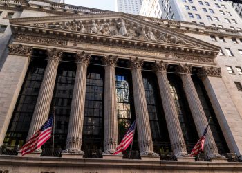 Iconic neoclassical facade of the New York Stock Exchange with American flags.