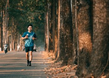 An athletic man runs along a picturesque tree-lined street during autumn. Perfect for fitness and outdoor themes.