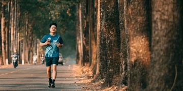 An athletic man runs along a picturesque tree-lined street during autumn. Perfect for fitness and outdoor themes.