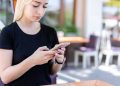 Young woman in a black shirt texting on her smartphone at an outdoor cafe.