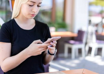 Young woman in a black shirt texting on her smartphone at an outdoor cafe.