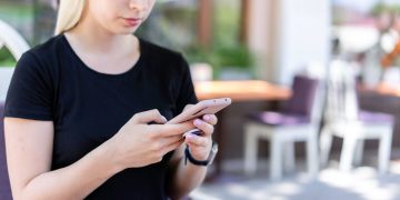 Young woman in a black shirt texting on her smartphone at an outdoor cafe.