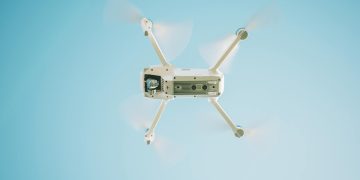 A sleek white drone flying under a clear blue sky, capturing aerial views.