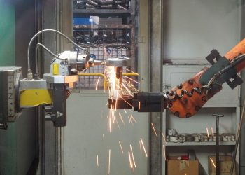 A robotic arm welding in an industrial setting, emitting bright sparks.