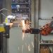 A robotic arm welding in an industrial setting, emitting bright sparks.