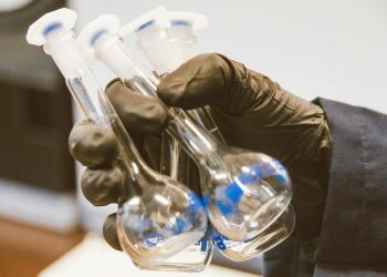 Gloved hand holding three empty laboratory flasks in a scientific setting.