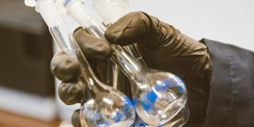 Gloved hand holding three empty laboratory flasks in a scientific setting.