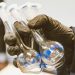 Gloved hand holding three empty laboratory flasks in a scientific setting.