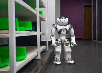 A humanoid robot standing in a modern corridor with shelves, representing futuristic technology.