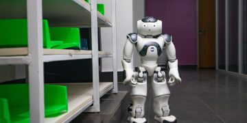 A humanoid robot standing in a modern corridor with shelves, representing futuristic technology.