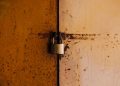 A close-up view of a rusty padlock securing a weathered metal door, highlighting decay and security.