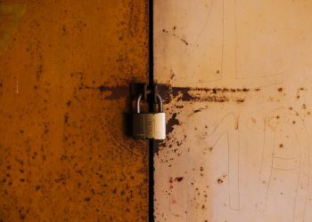 A close-up view of a rusty padlock securing a weathered metal door, highlighting decay and security.