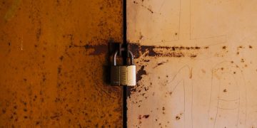 A close-up view of a rusty padlock securing a weathered metal door, highlighting decay and security.