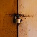 A close-up view of a rusty padlock securing a weathered metal door, highlighting decay and security.
