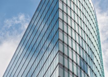 A sleek glass skyscraper reflecting the blue sky and clouds, showcasing modern architectural design.