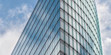 A sleek glass skyscraper reflecting the blue sky and clouds, showcasing modern architectural design.