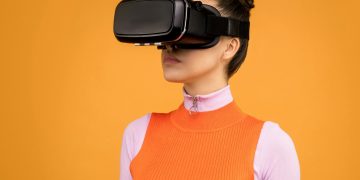 Woman enjoying virtual reality with VR headset against vibrant orange background.