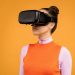Woman enjoying virtual reality with VR headset against vibrant orange background.