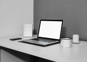 A modern minimalistic desk setup with a laptop, ceramic cup, and candle for a serene workspace.
