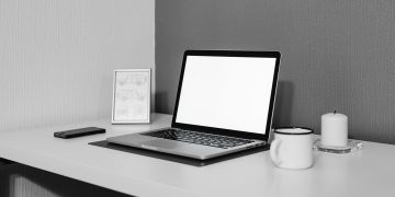 A modern minimalistic desk setup with a laptop, ceramic cup, and candle for a serene workspace.