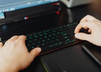 Closeup of hands typing on an RGB keyboard in a modern office setting.