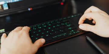 Closeup of hands typing on an RGB keyboard in a modern office setting.