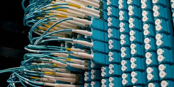 Detailed view of fiber optic patch cables connecting to a blue patch panel in a data center.