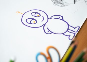 Colorful cartoon character sketch on paper with colored pencils on the side.