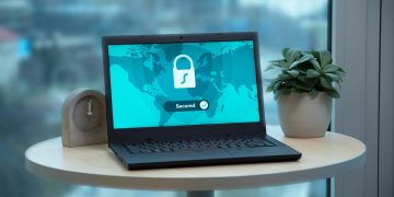 Laptop displaying a security lock icon on a table with a potted plant and clock.