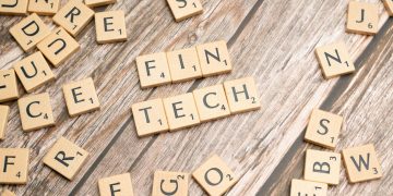 Fintech spelled out with wooden letter tiles on a rustic wooden background.