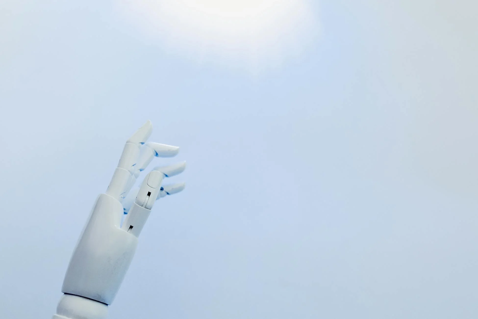 A robotic hand reaching towards a bright light on a white background symbolizing innovation.