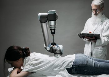 A woman receives a robotic massage as a scientist monitors, showcasing modern technology.
