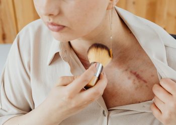Close-up of a woman using a brush to cover a chest scar with makeup.