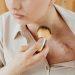 Close-up of a woman using a brush to cover a chest scar with makeup.