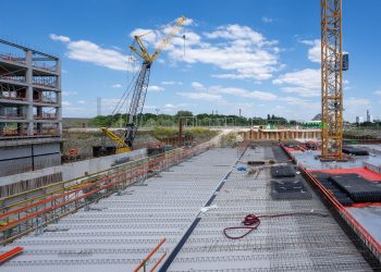 View of a busy construction site with cranes and building structure under clear sky.
