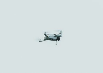 A single drone flying against a clear, pale sky in a minimalist composition.