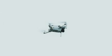 A single drone flying against a clear, pale sky in a minimalist composition.