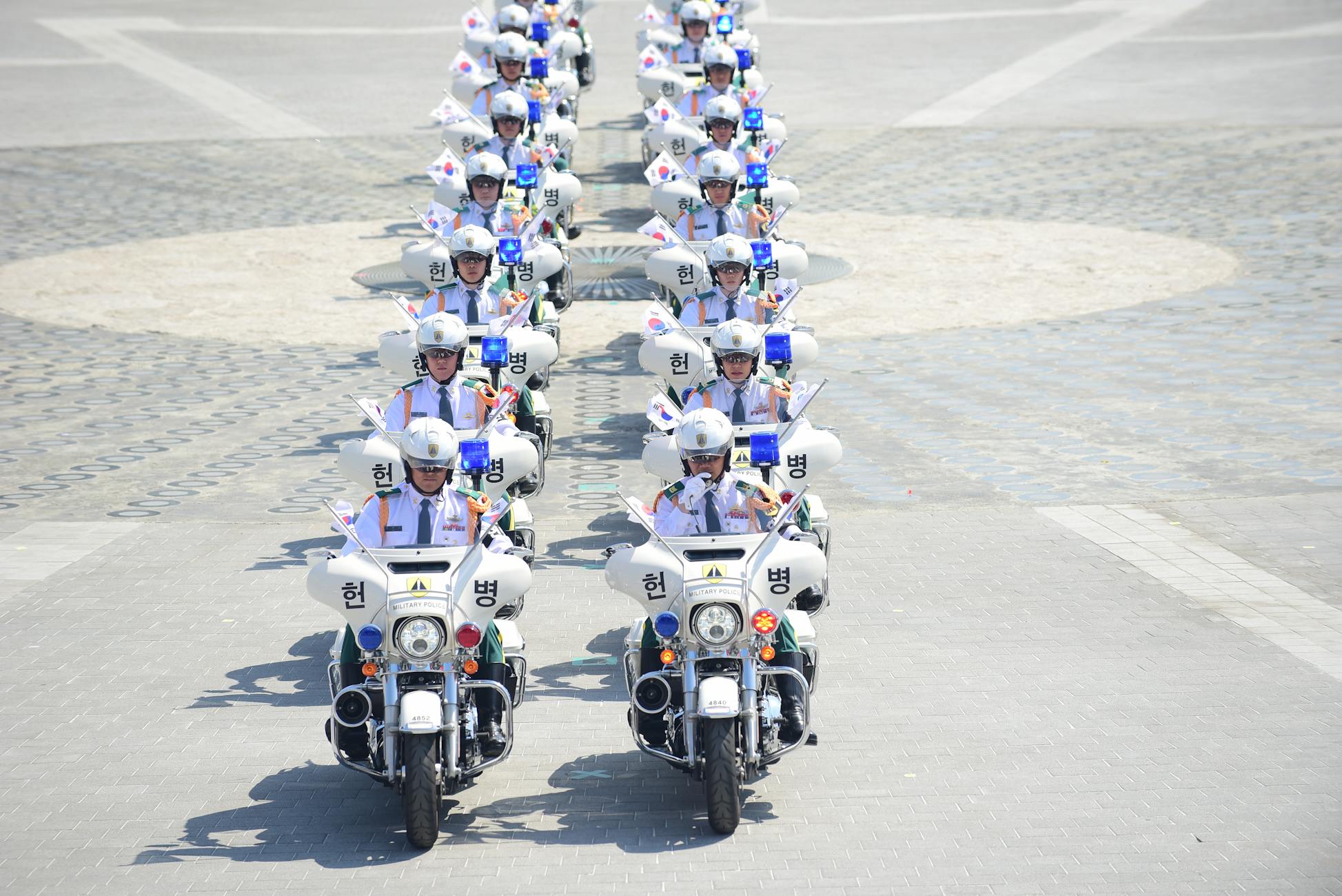 A line of South Korean police officers on motorcycles holding flags in an urban parade.