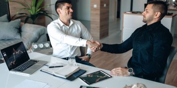 Two businessmen shaking hands in an office, symbolizing a successful business agreement.