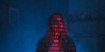 A mysterious silhouette with red binary code projected over the face, set against a dark, moody background.