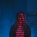 A mysterious silhouette with red binary code projected over the face, set against a dark, moody background.
