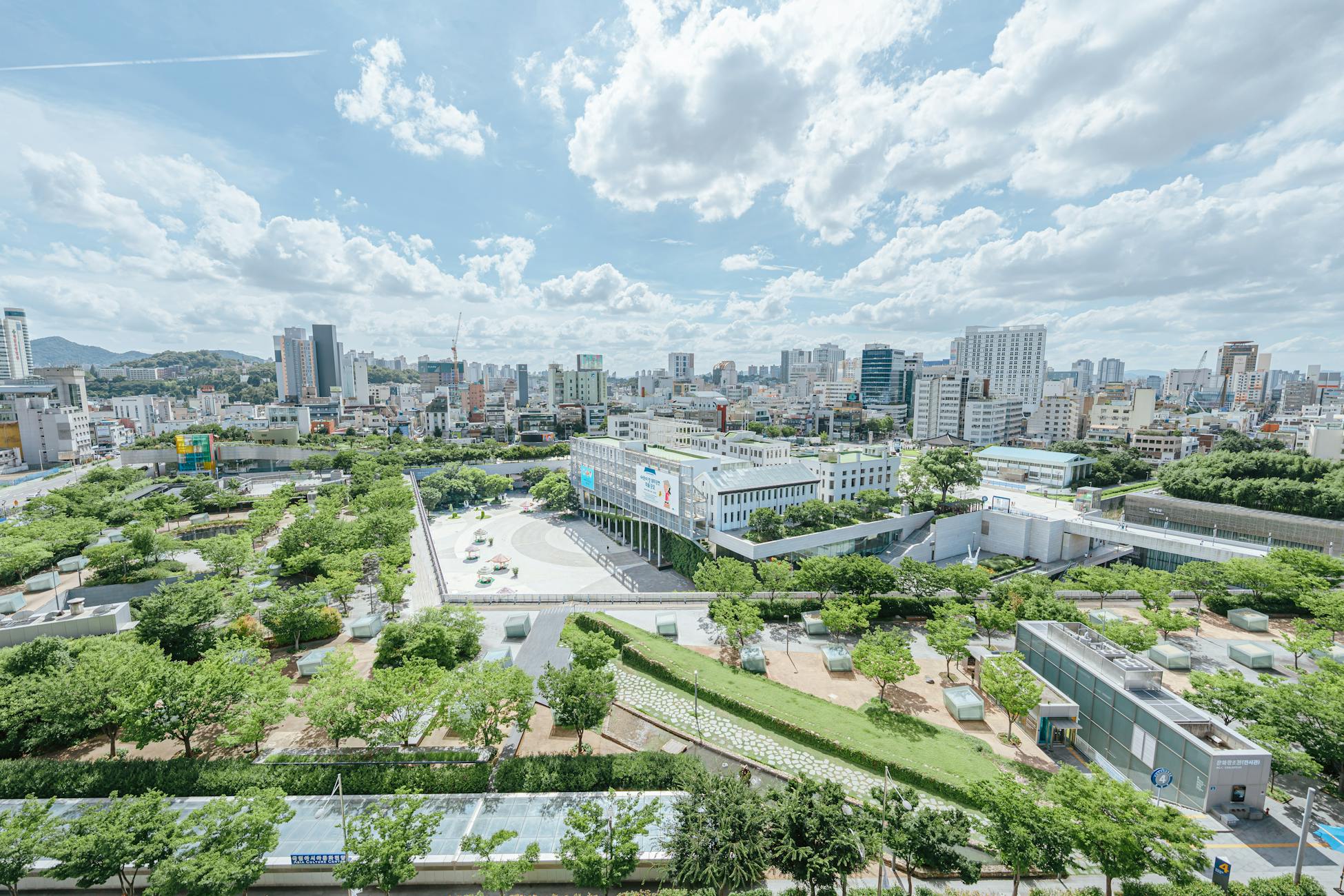Aerial shot of a modern city with green parks, cloudy sky, and high-rise buildings.