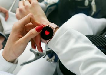 Close-up of a woman's hand with red nails interacting with a smartwatch displaying a heart icon.
