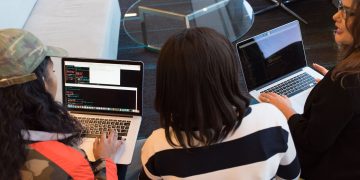 Three women working on laptops in a stylish office, focused on a collaborative project.