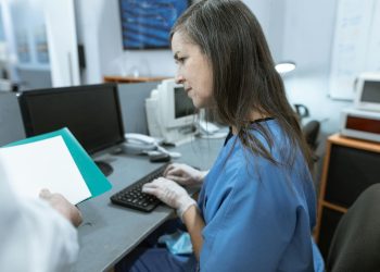 Nurse in scrubs typing on a keyboard at a medical workstation.